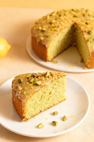 Ein St&uuml;ck Pistazien-Zitronenkuchen auf einem Teller, bestreut mit gehackten Pistazien und Zitronenzeste.